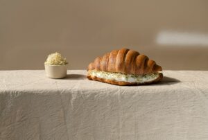 a croissant sandwich on a table next to a small bowl of cottage cheese